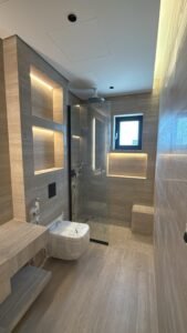 Modern luxury villa bathroom with glass shower, stone finish tiles and warm LED lighting ( residential construction project saudi arabia)