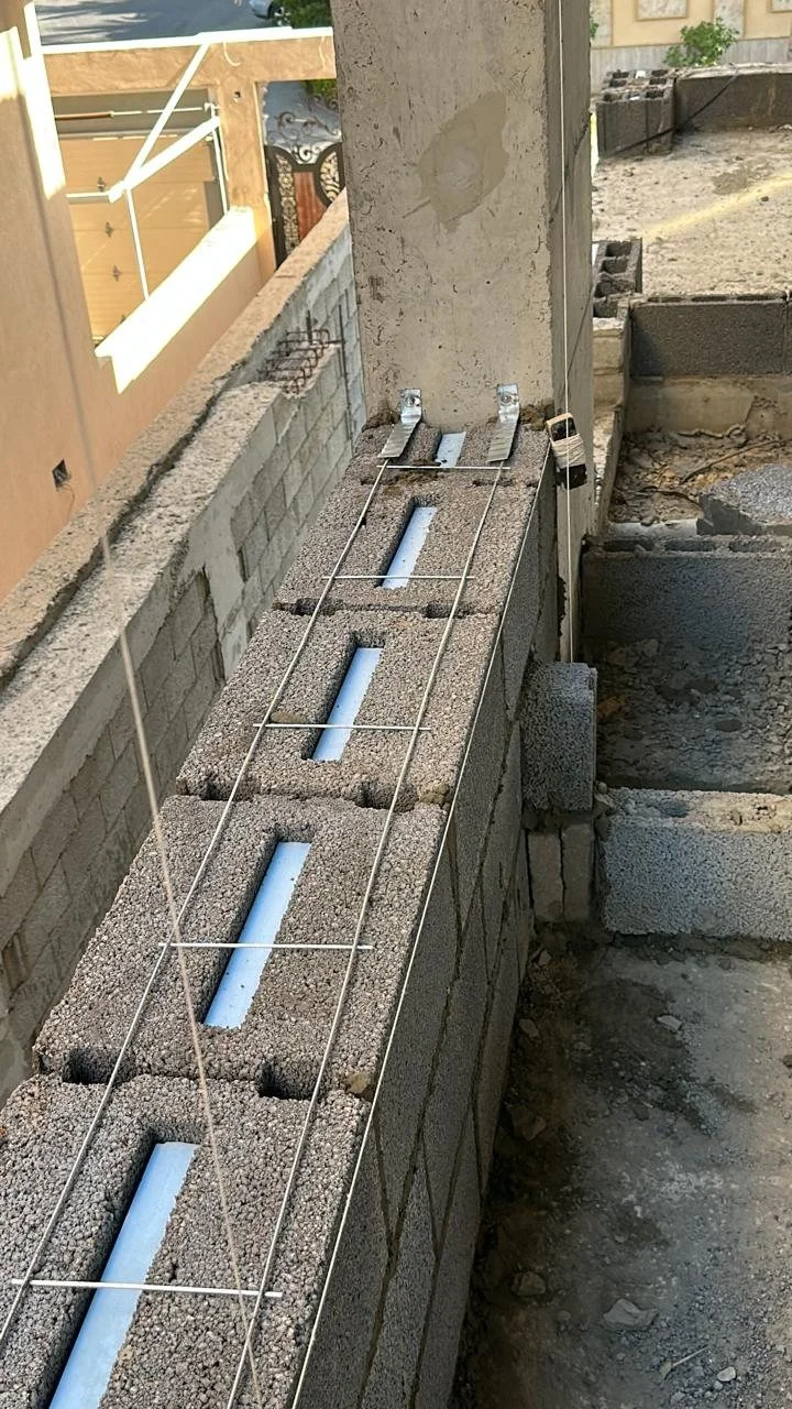 Steel reinforcement laid along a block wall course, with ties fixed to the concrete column